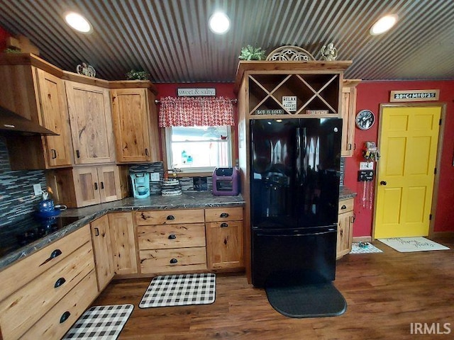 kitchen with dark wood finished floors, dark stone countertops, wall chimney range hood, black appliances, and recessed lighting