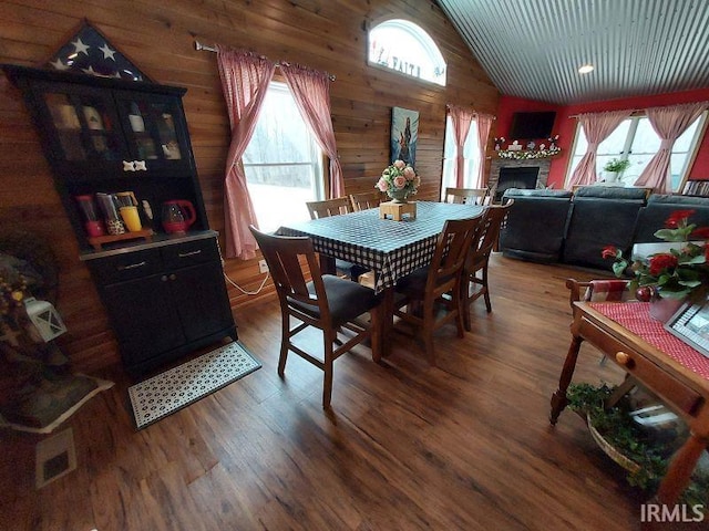 dining room featuring a healthy amount of sunlight, wood walls, wood finished floors, and lofted ceiling