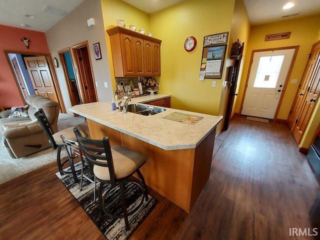 kitchen with brown cabinetry, dark wood finished floors, a peninsula, light countertops, and a sink