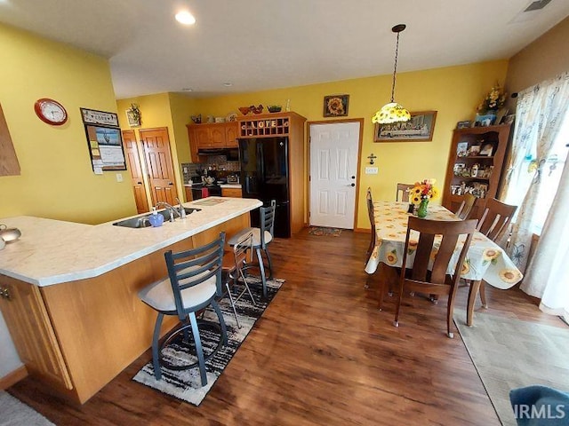 kitchen with brown cabinetry, hanging light fixtures, light countertops, black appliances, and a sink