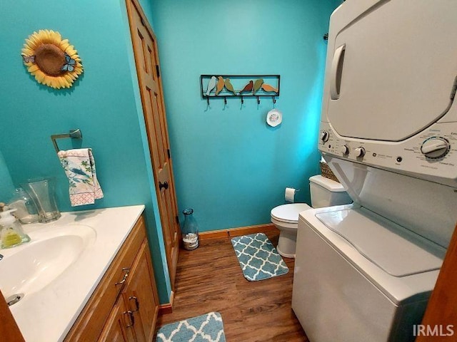 bathroom featuring stacked washer and clothes dryer, toilet, vanity, wood finished floors, and baseboards