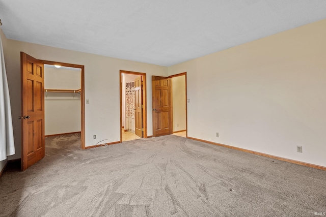 unfurnished bedroom with a walk in closet, a closet, light carpet, and baseboards