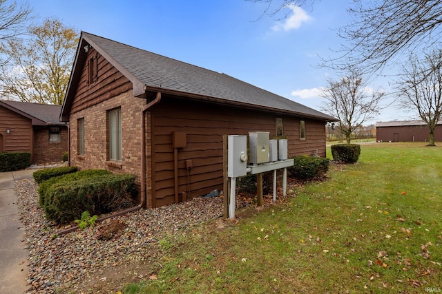 view of property exterior featuring a shingled roof, a lawn, and brick siding