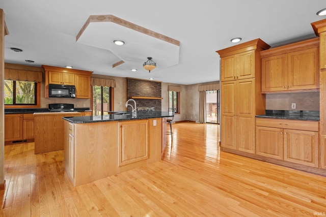 kitchen with a breakfast bar area, stove, light wood-style floors, an island with sink, and black microwave