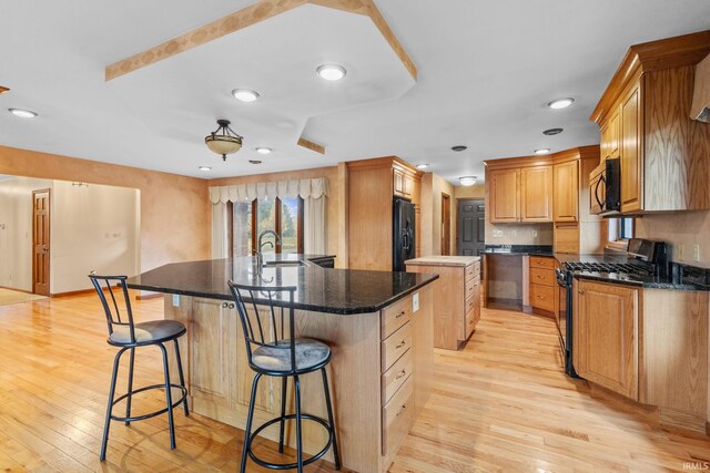 kitchen featuring range with gas stovetop, black fridge, stainless steel microwave, a kitchen bar, and a center island with sink