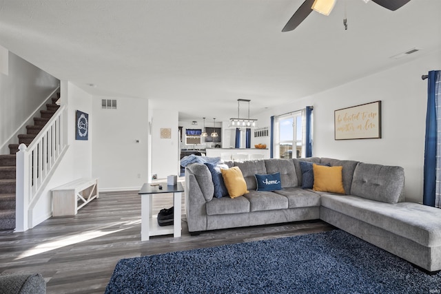 living room featuring baseboards, visible vents, stairway, wood finished floors, and ceiling fan with notable chandelier