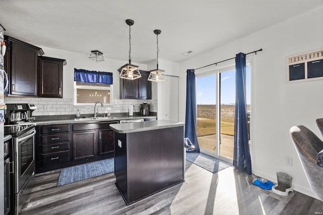 kitchen with pendant lighting, stainless steel electric stove, backsplash, a kitchen island, and a sink