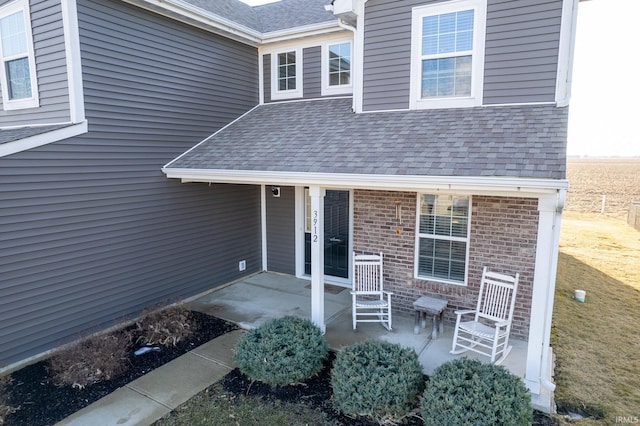 property entrance with a patio, a shingled roof, and brick siding