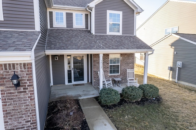 doorway to property featuring brick siding, roof with shingles, and a porch