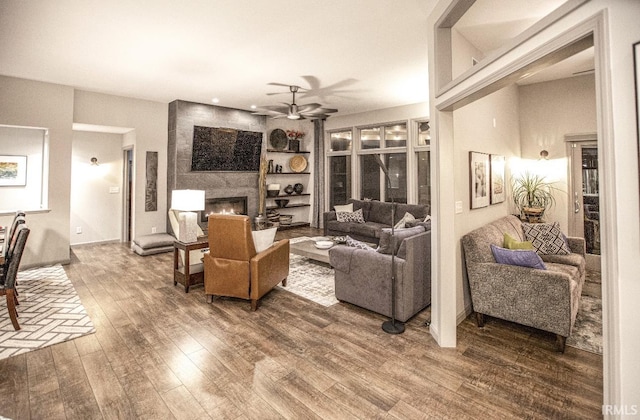 living room featuring a large fireplace, ceiling fan, and wood finished floors