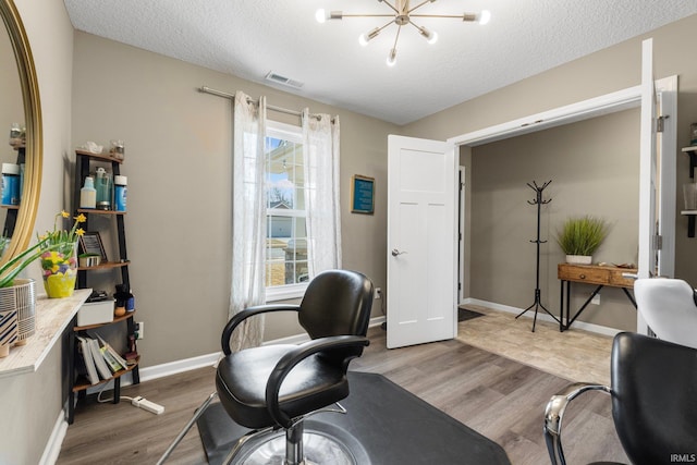 office space with a notable chandelier, visible vents, a textured ceiling, wood finished floors, and baseboards