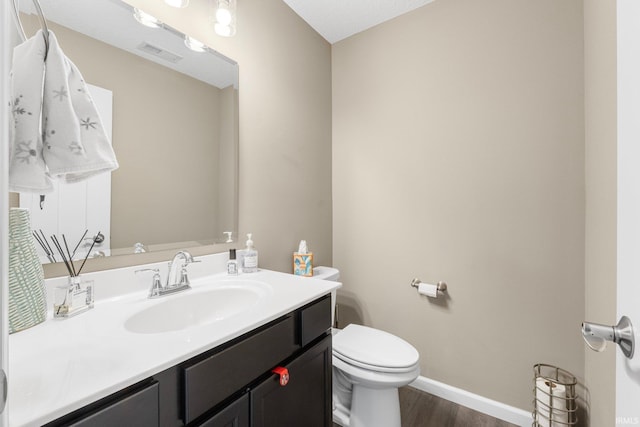 bathroom with toilet, wood finished floors, vanity, visible vents, and baseboards