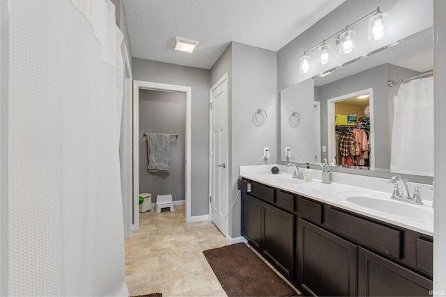 bathroom with a textured ceiling, double vanity, a sink, and a walk in closet