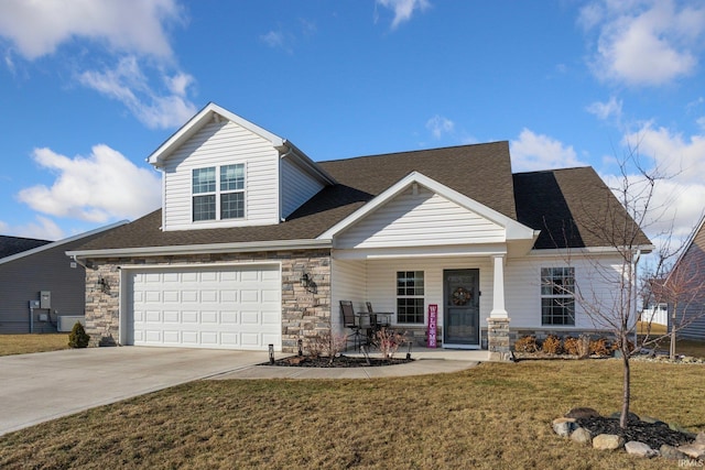 view of front of property featuring a front yard, stone siding, roof with shingles, and driveway