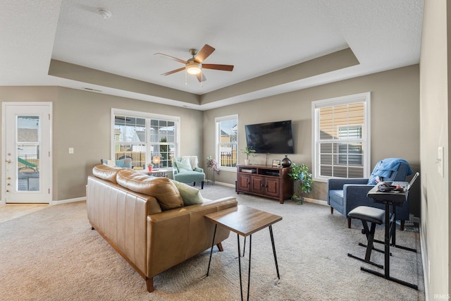 living area with a textured ceiling, light carpet, a ceiling fan, baseboards, and a tray ceiling