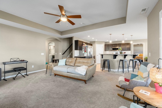 living room featuring baseboards, visible vents, arched walkways, light colored carpet, and stairway