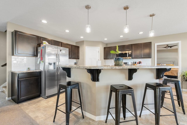 kitchen featuring dark brown cabinetry, a kitchen island, a breakfast bar, decorative light fixtures, and stainless steel appliances