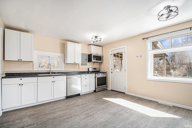 kitchen featuring a sink, white cabinets, appliances with stainless steel finishes, light wood-type flooring, and dark countertops