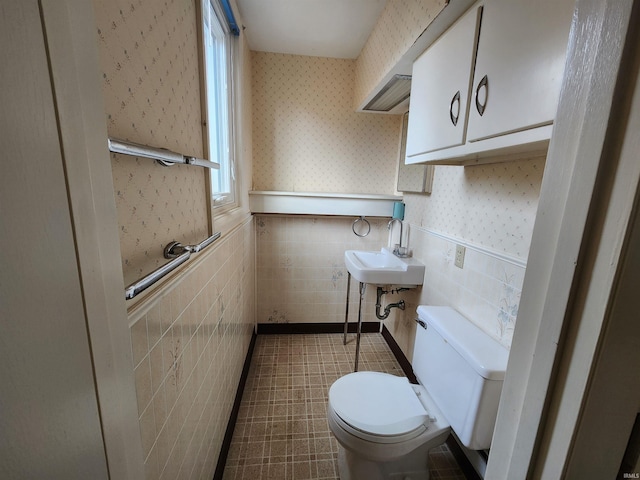 bathroom with tile walls, wainscoting, toilet, and wallpapered walls