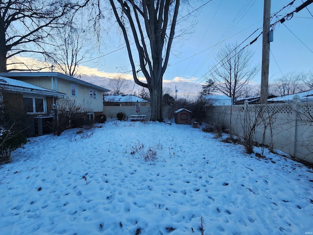 yard covered in snow featuring central air condition unit, a storage shed, fence, and an outdoor structure