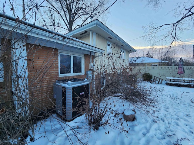 view of snowy exterior featuring fence, a mountain view, central AC, and brick siding