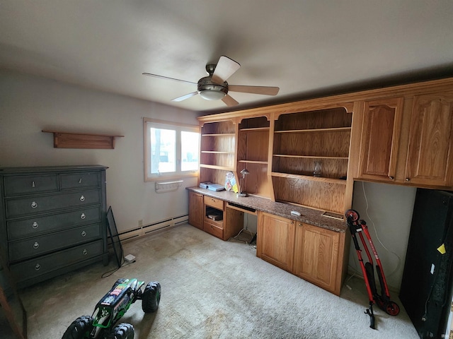 unfurnished office with a baseboard heating unit, built in desk, light carpet, and a ceiling fan