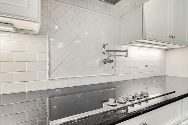 kitchen with dark countertops, white cabinetry, backsplash, and stovetop