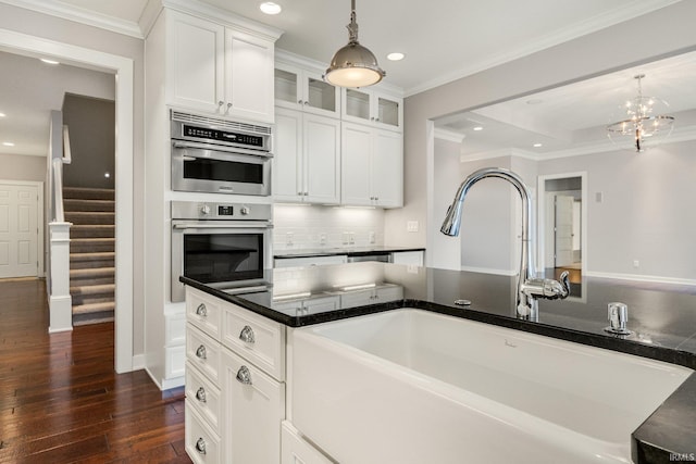 kitchen with a sink, white cabinetry, dark countertops, glass insert cabinets, and pendant lighting