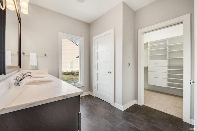 full bathroom featuring double vanity, a spacious closet, a sink, and baseboards