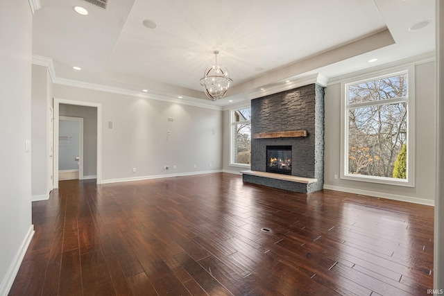 unfurnished living room featuring a stone fireplace, a tray ceiling, dark wood finished floors, and baseboards