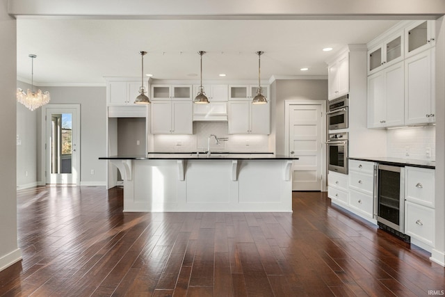 kitchen with dark countertops, wine cooler, glass insert cabinets, and an island with sink