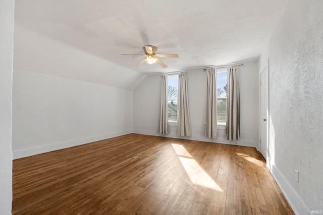 additional living space featuring baseboards, a textured wall, hardwood / wood-style flooring, ceiling fan, and vaulted ceiling