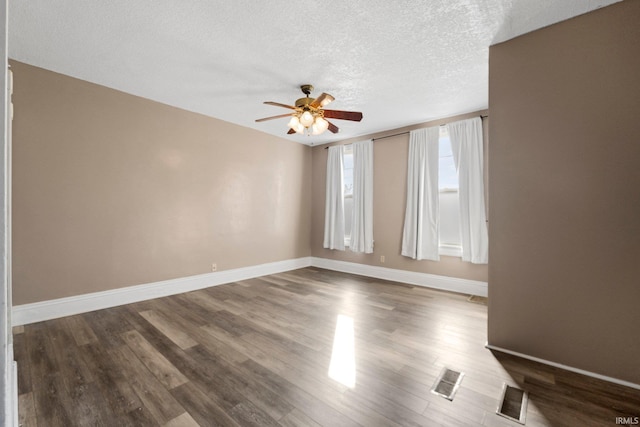 empty room featuring ceiling fan, a textured ceiling, dark wood-type flooring, visible vents, and baseboards