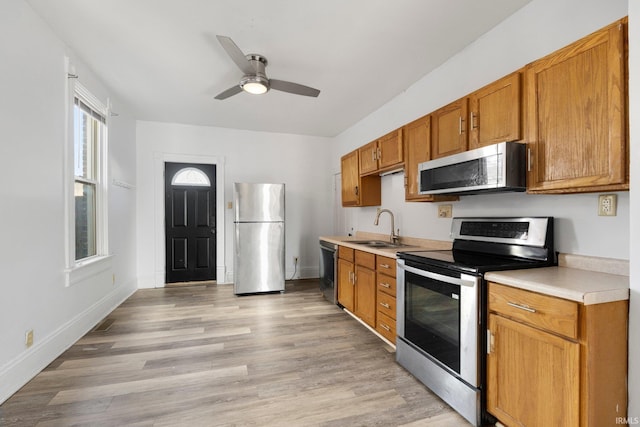 kitchen featuring a sink, light countertops, appliances with stainless steel finishes, light wood finished floors, and brown cabinetry