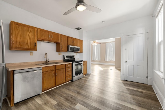 kitchen featuring wood finished floors, a sink, light countertops, appliances with stainless steel finishes, and brown cabinetry