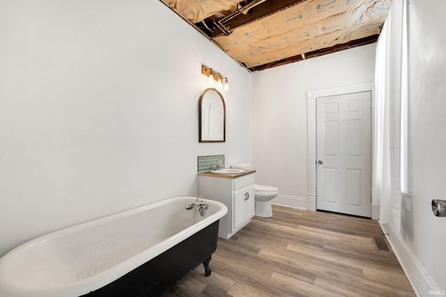 full bath with a freestanding bath, toilet, vanity, wood finished floors, and baseboards