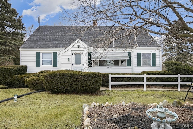 cape cod home featuring a front yard, roof with shingles, fence, and a chimney