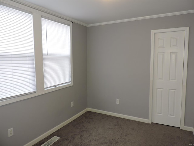 empty room with dark colored carpet, ornamental molding, visible vents, and baseboards