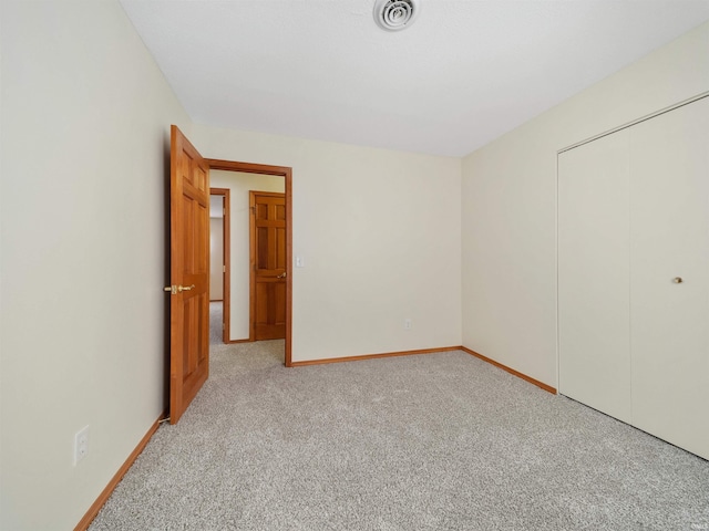 unfurnished bedroom featuring light carpet, baseboards, visible vents, and a closet