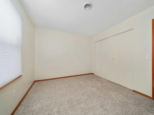 unfurnished bedroom featuring light carpet, a closet, visible vents, and baseboards