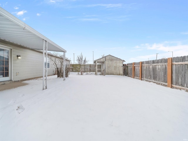 snowy yard featuring a storage shed, an outdoor structure, and a fenced backyard