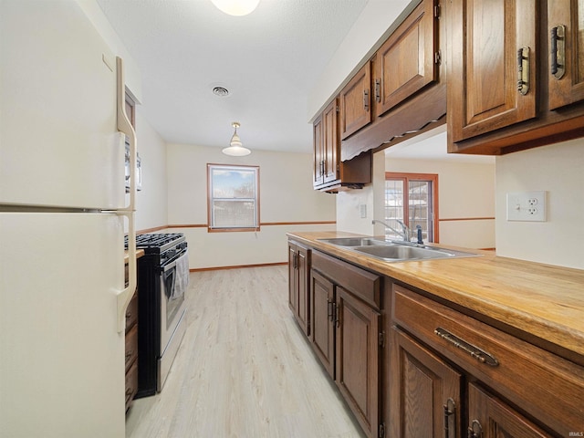 kitchen featuring freestanding refrigerator, a sink, gas range, light wood-type flooring, and plenty of natural light