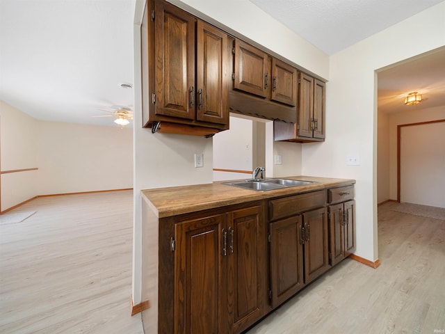 kitchen featuring a sink, a ceiling fan, baseboards, light wood-style floors, and dark brown cabinets