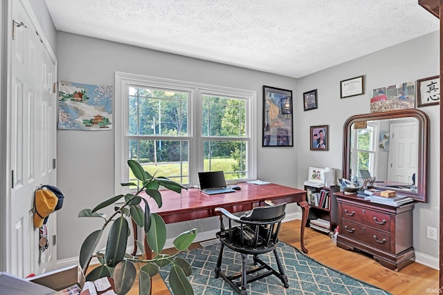 office area with light wood-style flooring, baseboards, and a textured ceiling