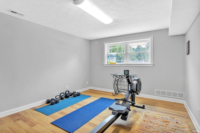 exercise area featuring wood finished floors, visible vents, and baseboards