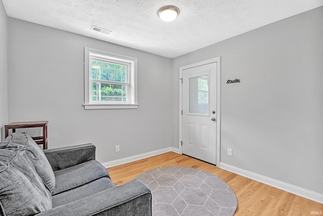 entryway with a textured ceiling, wood finished floors, visible vents, and baseboards