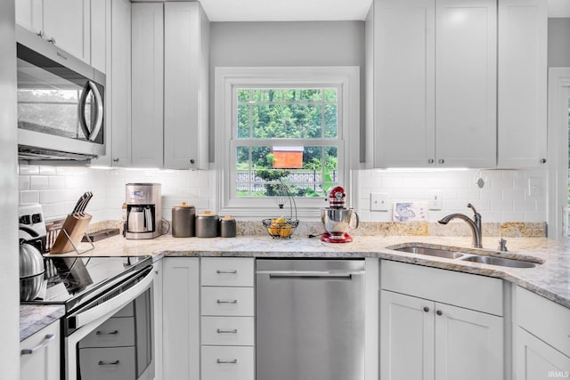 kitchen with stainless steel appliances, white cabinetry, a sink, and light stone counters