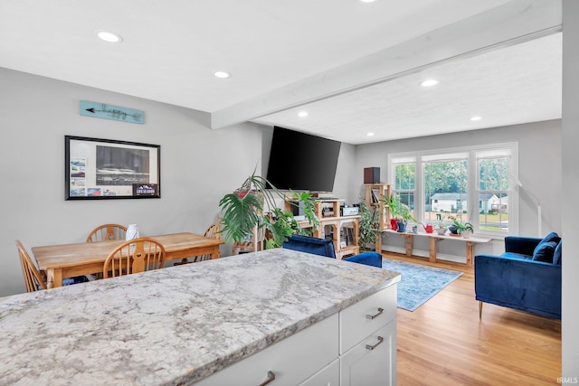 kitchen featuring beam ceiling, light wood finished floors, open floor plan, white cabinets, and light stone countertops