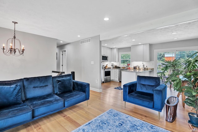 living room featuring a chandelier, light wood-style flooring, recessed lighting, visible vents, and baseboards