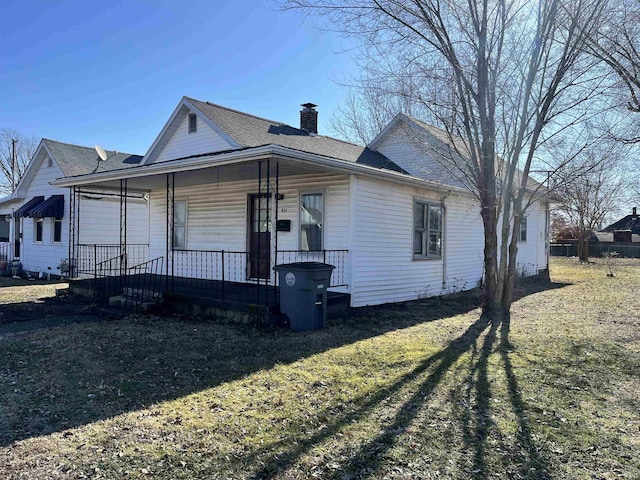 view of front of home with a porch, a front yard, a shingled roof, and a chimney